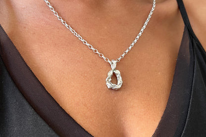 Silver necklace with an initial letter pendant on a person.