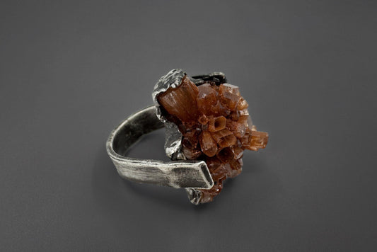 Silver ring with a brown aragonite crystal on a dark gray background